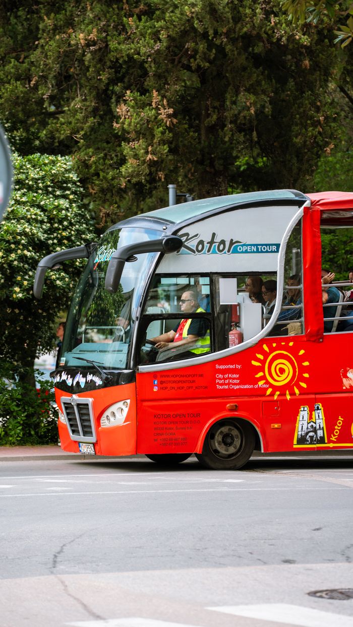 gallery-1 Red open tour bus in Kotor, Montenegro, showcasing scenic travel opportunities.