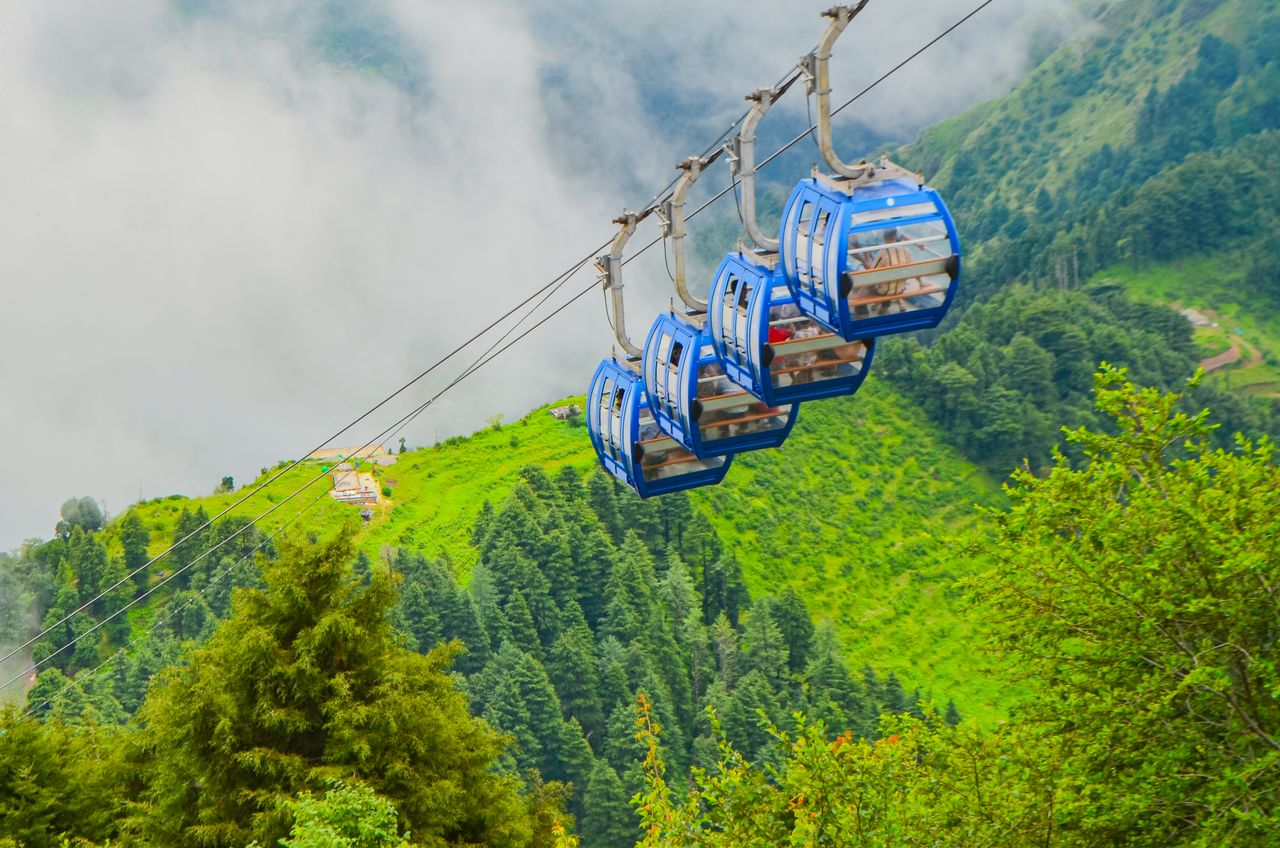 why-choose-us Breathtaking view of cable cars gliding over lush green mountainous landscape with mist.